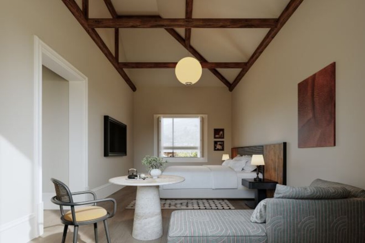 A bedroom with a bed, bedside table, lamp, chair, and a view of the outdoors.