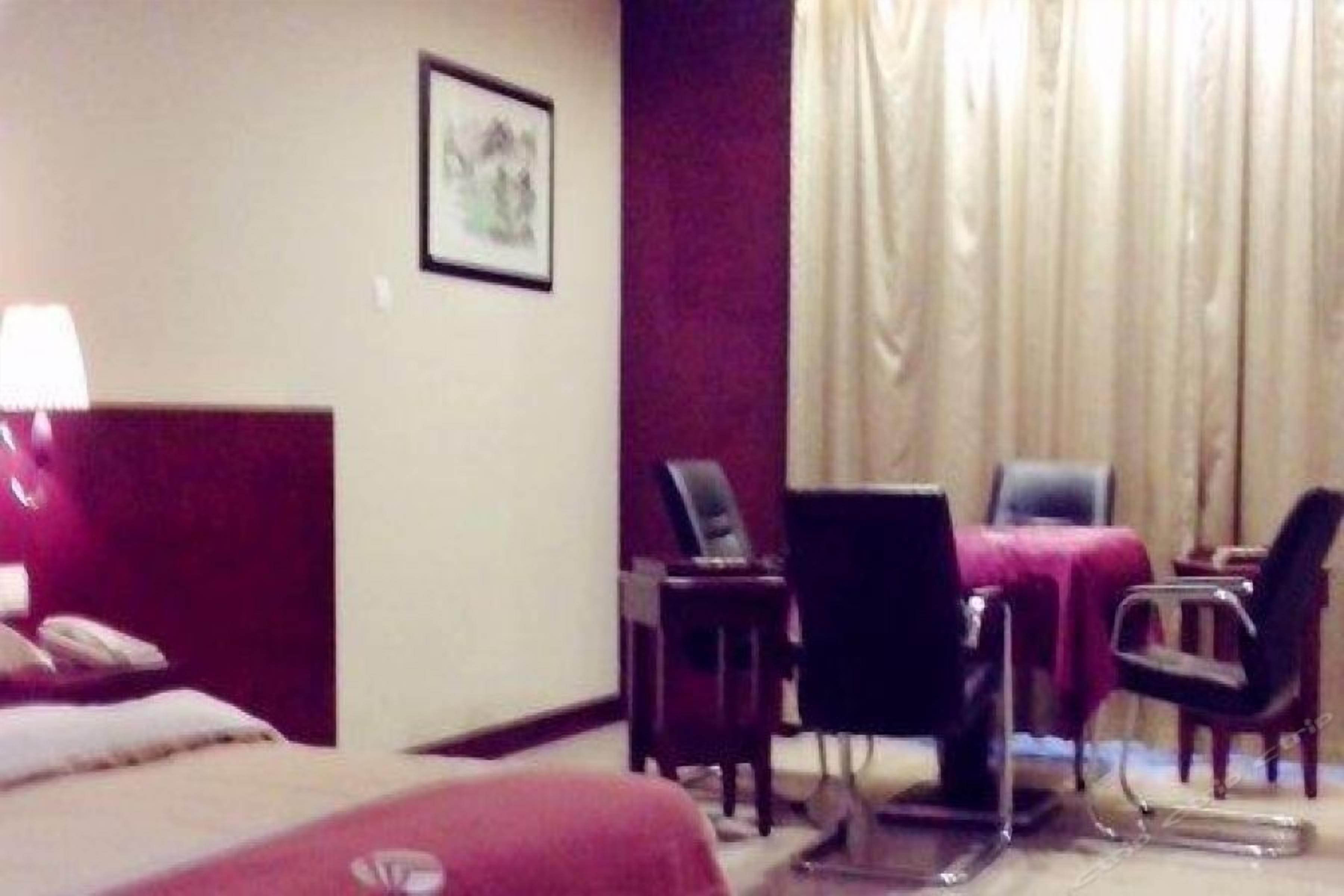 A hotel room with a bed, a desk, two chairs, a lamp, and a window with curtains.
