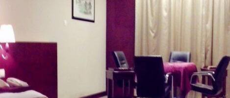 Una habitación de hotel con una cama, un escritorio, dos sillas, una lámpara y una ventana con cortinas.