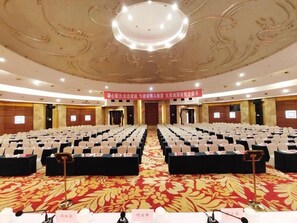 Een congreszaal met rijen stoelen, een podium en een vloerbedekking.