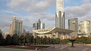 A modern cityscape with a prominent skyscraper, a unique building with a curved roof, and surrounding high-rise buildings.