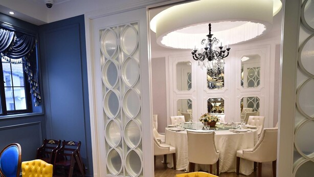 A dining area with a round table set for four, surrounded by white upholstered chairs.