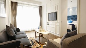 A hotel room with a sofa, a small table with a tray, a TV, and a bed with a blue headboard.