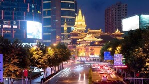 A nighttime cityscape with traditional architecture in the foreground and modern buildings in the background.