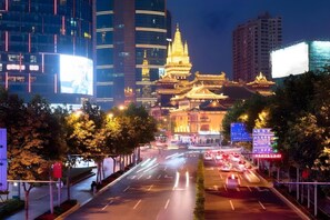 A nighttime cityscape with traditional architecture in the foreground and modern buildings in the background.