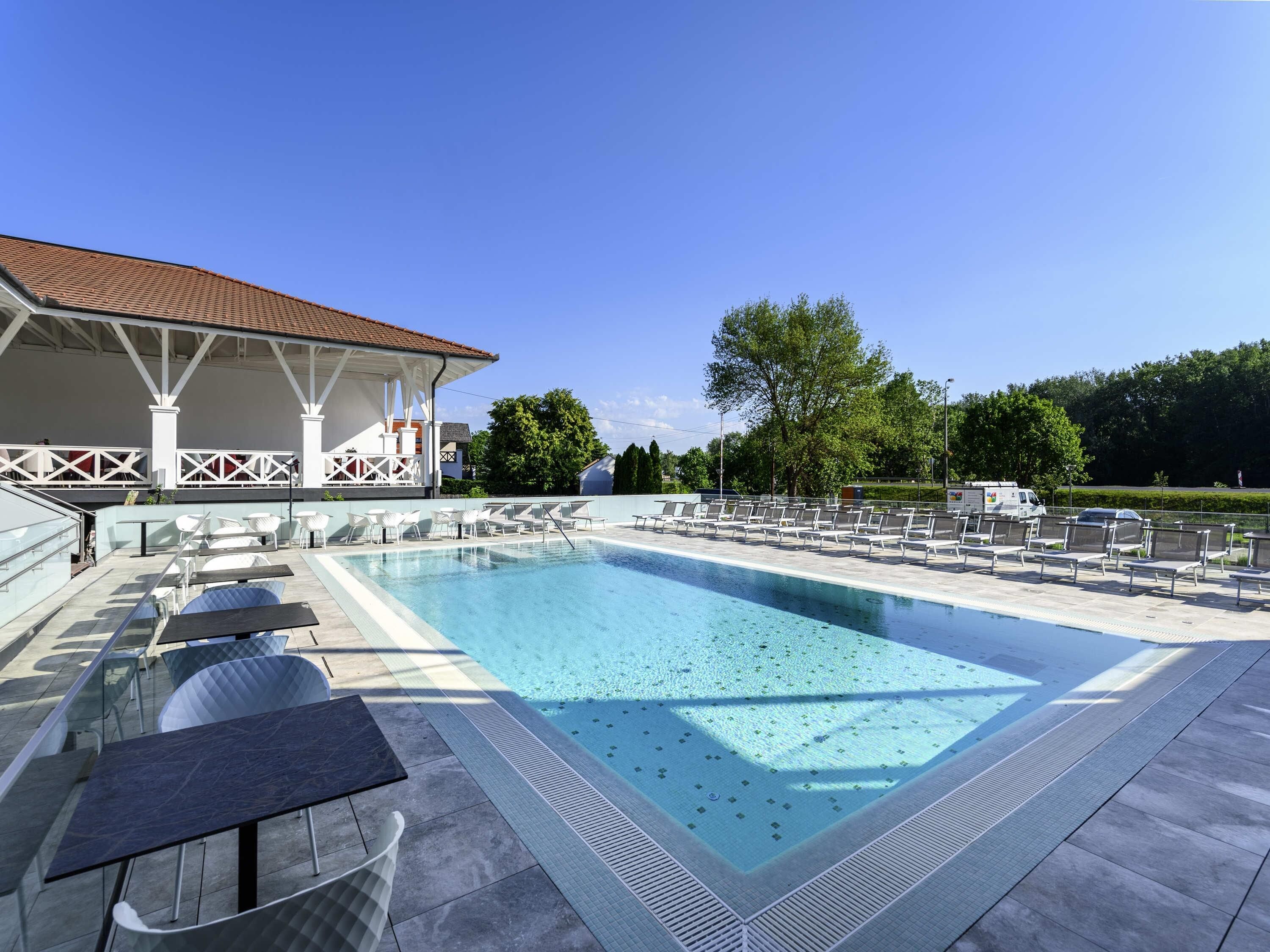 A swimming pool with lounge chairs, a covered seating area, and a building with a tiled roof.
