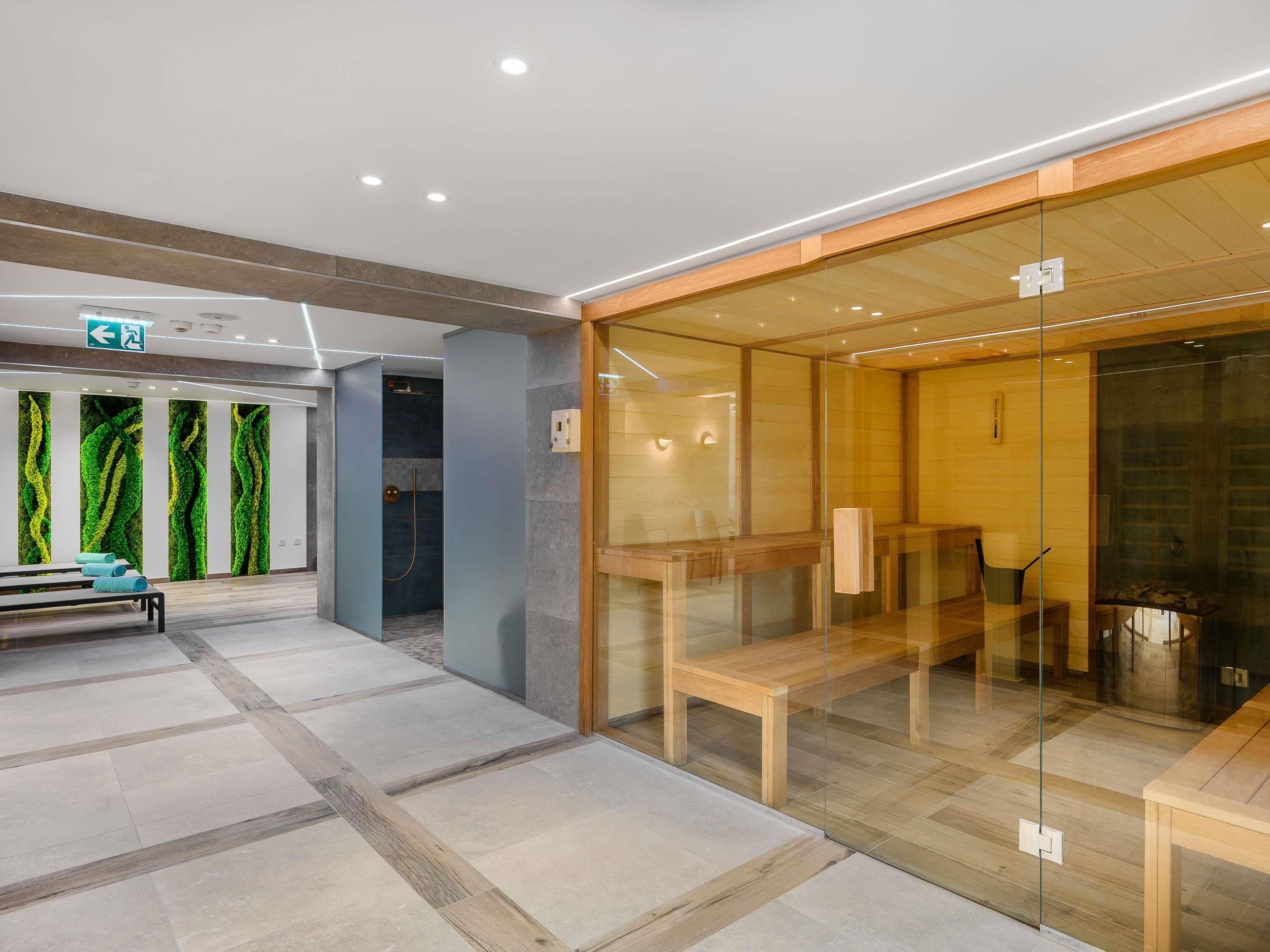 Un moderno vestíbulo de hotel con un separador de vidrio, bancos de madera y una recepción con diseño de pared verde.