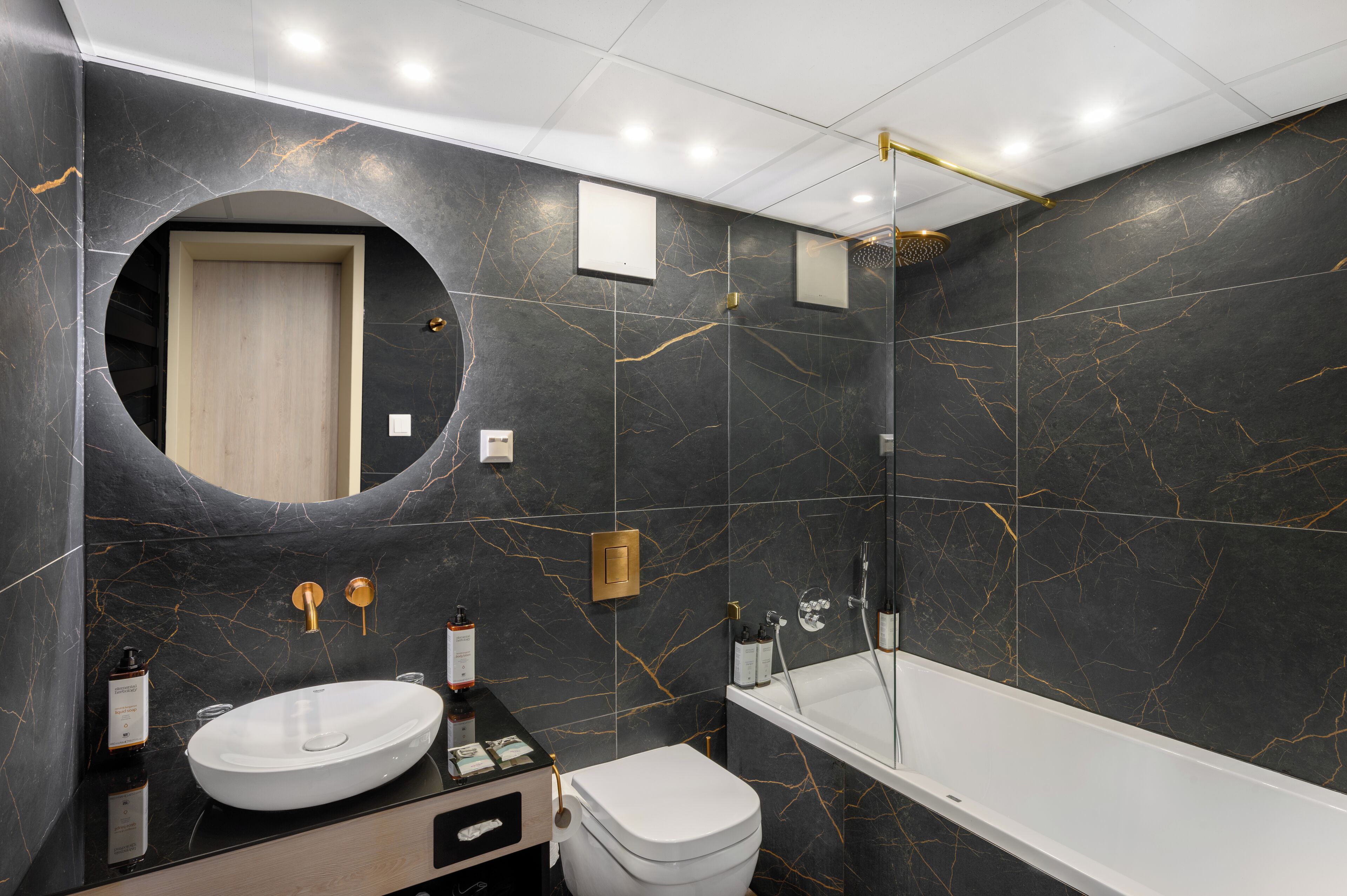 A modern bathroom with a round mirror, a white sink, a toilet, and a bathtub.