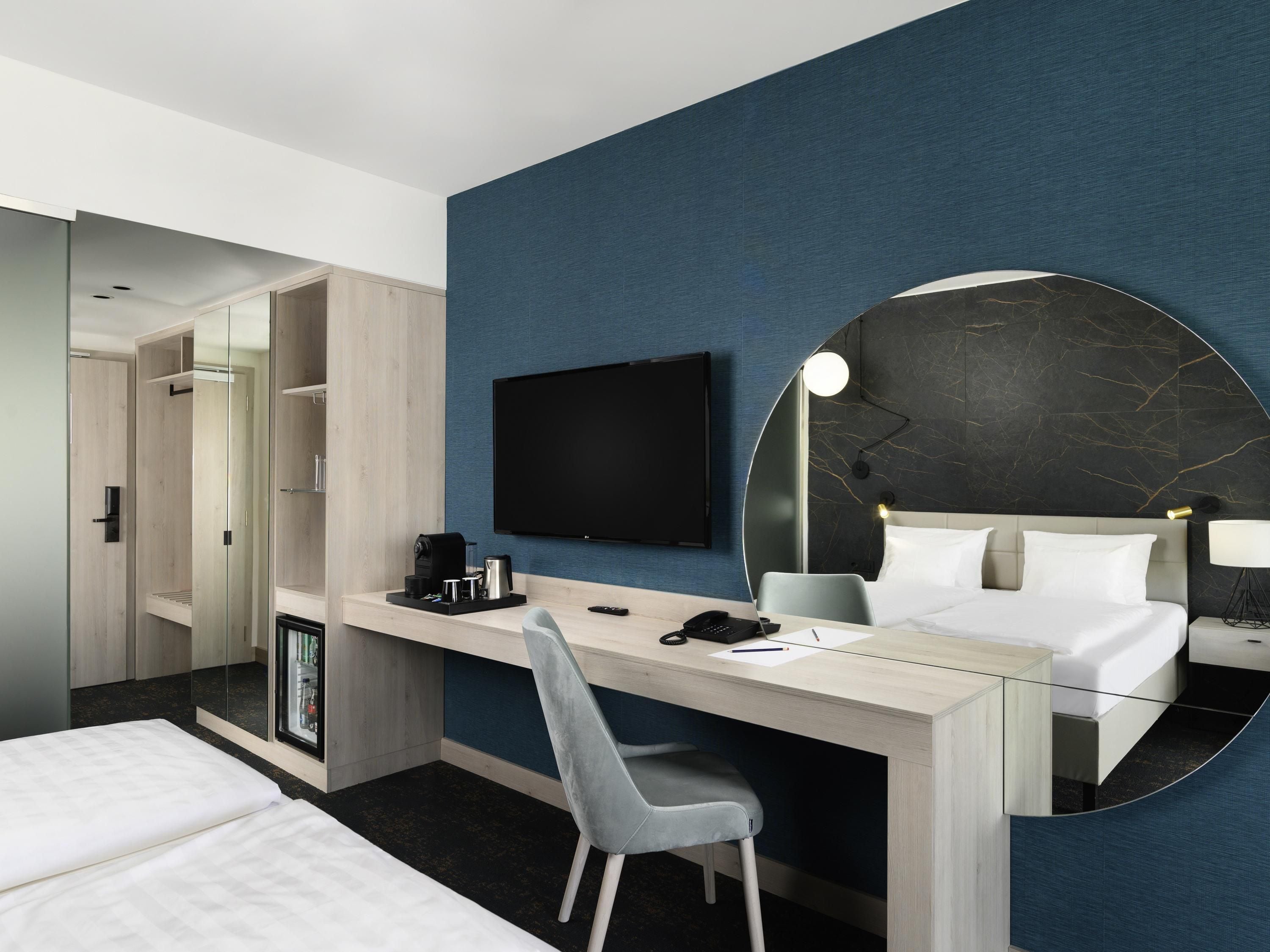 Una habitación de hotel moderna con cama, escritorio, silla y un espejo grande.