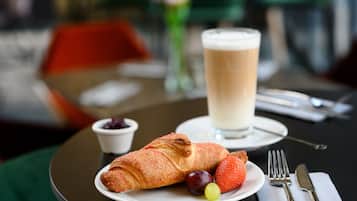 Una mesa con un croissant, fresas, uvas y un vaso de leche.