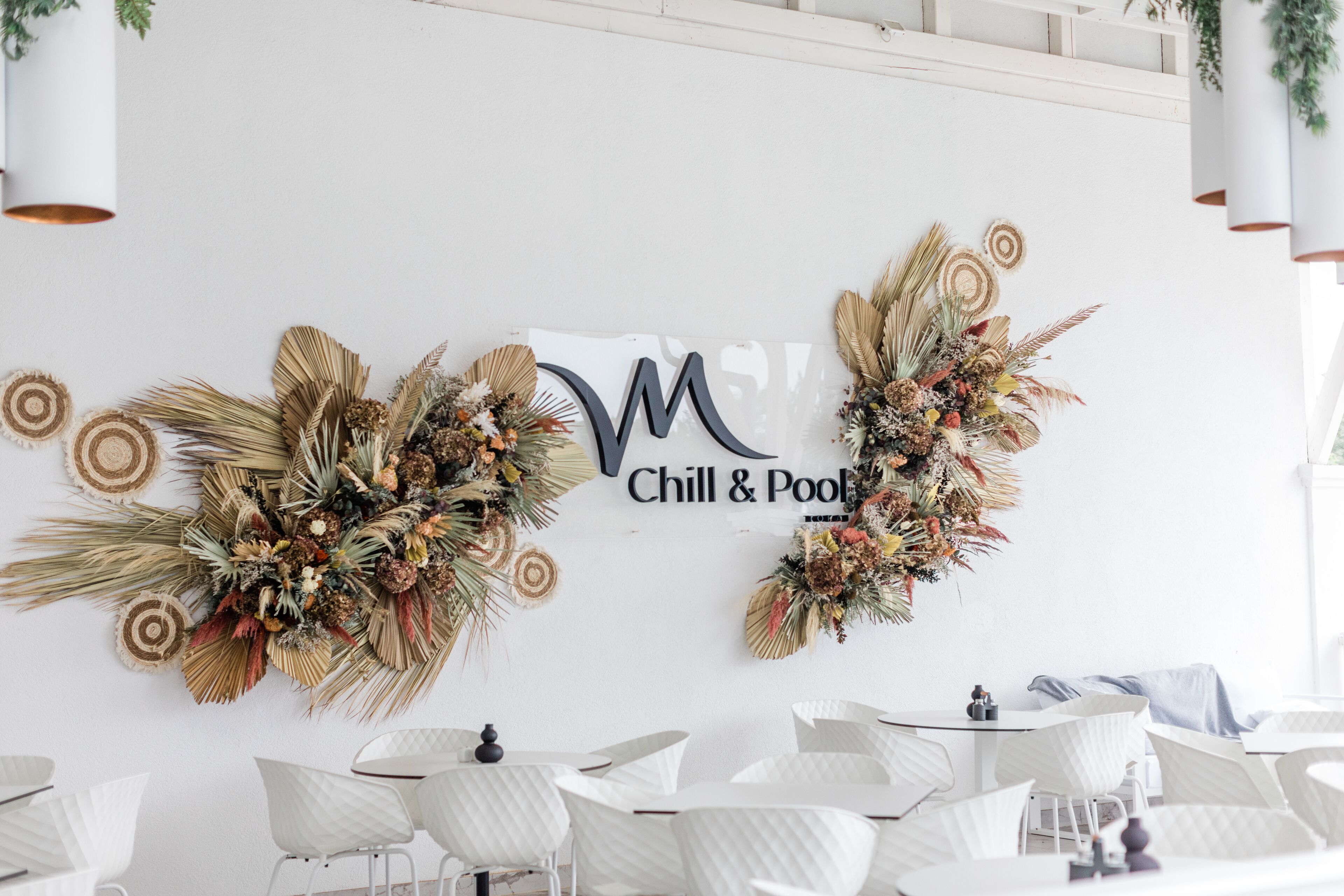 A room with white chairs, a 'Chill & Pool' sign, and decorative wall art.