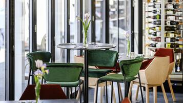 A modern cafe with round tables, green and red chairs, and a wine display in the background.