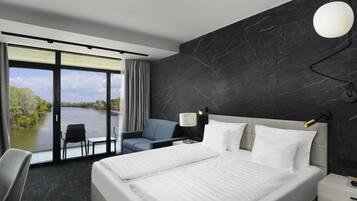 Een moderne hotelkamer met een groot bed, een bureau met stoel, uitzicht op een rivier en een donkere marmeren wand.