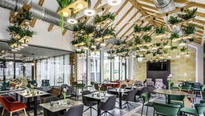 A modern restaurant with multiple dining areas, wooden ceiling beams, hanging plants, and large windows. - Mercure Tokaj Center (Tokaj)
