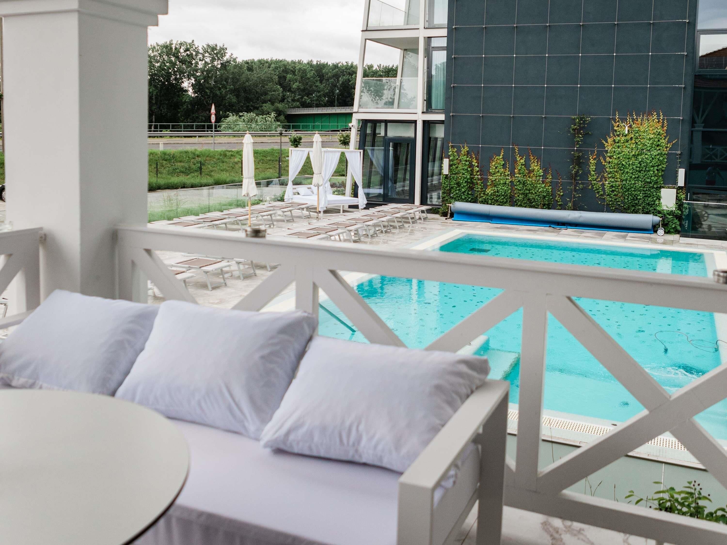 Zona junto a la piscina con un deck blanco, sillas de descanso y vistas a un edificio de diseño moderno.
