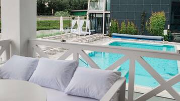 Zona junto a la piscina con un deck blanco, sillas de descanso y vistas a un edificio de diseño moderno.