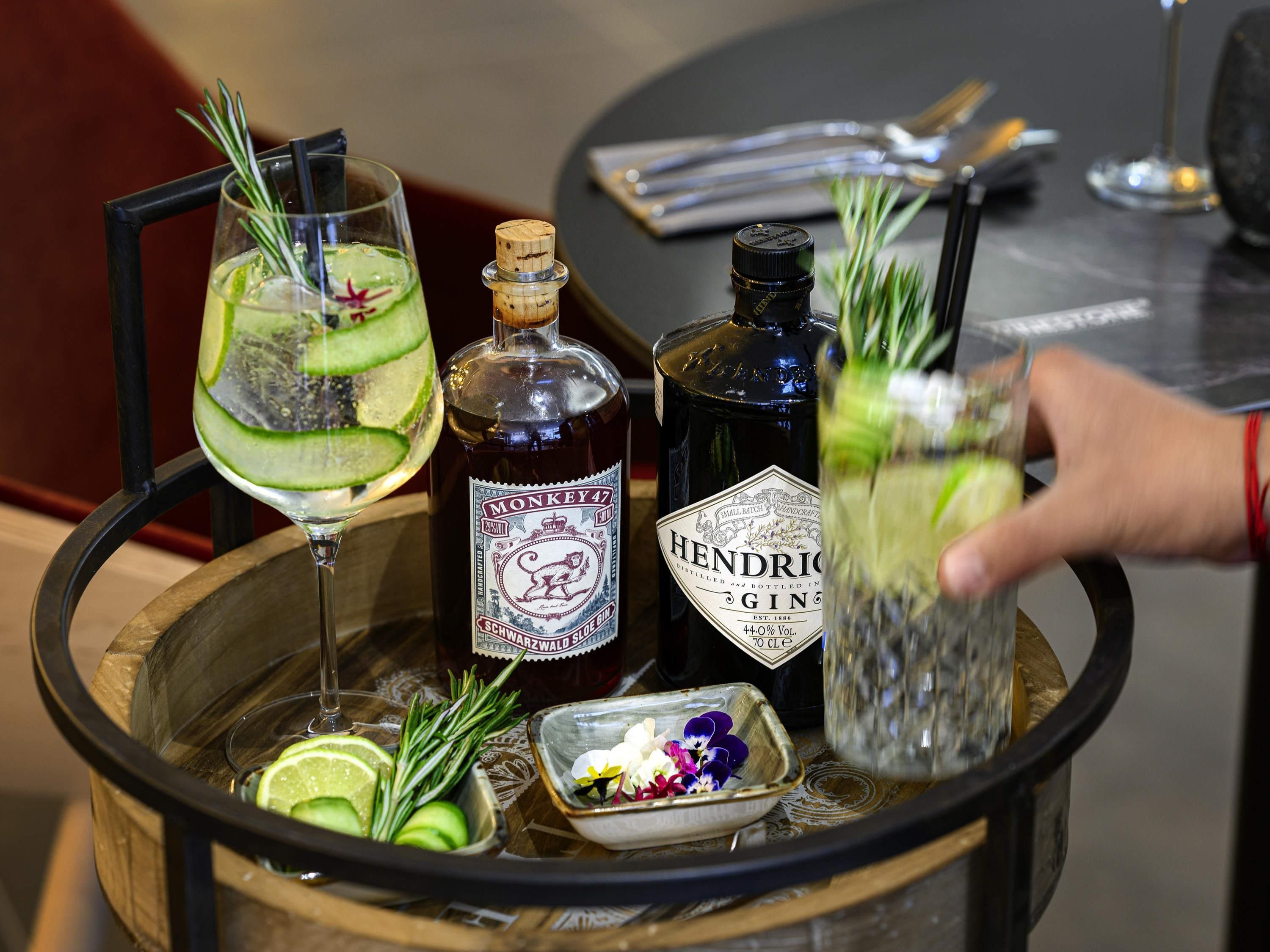 Una zona de bar con una botella de ginebra Hendrick's, un vaso con una rodaja de pepino y una pajita, y un pequeño cuenco con flores.