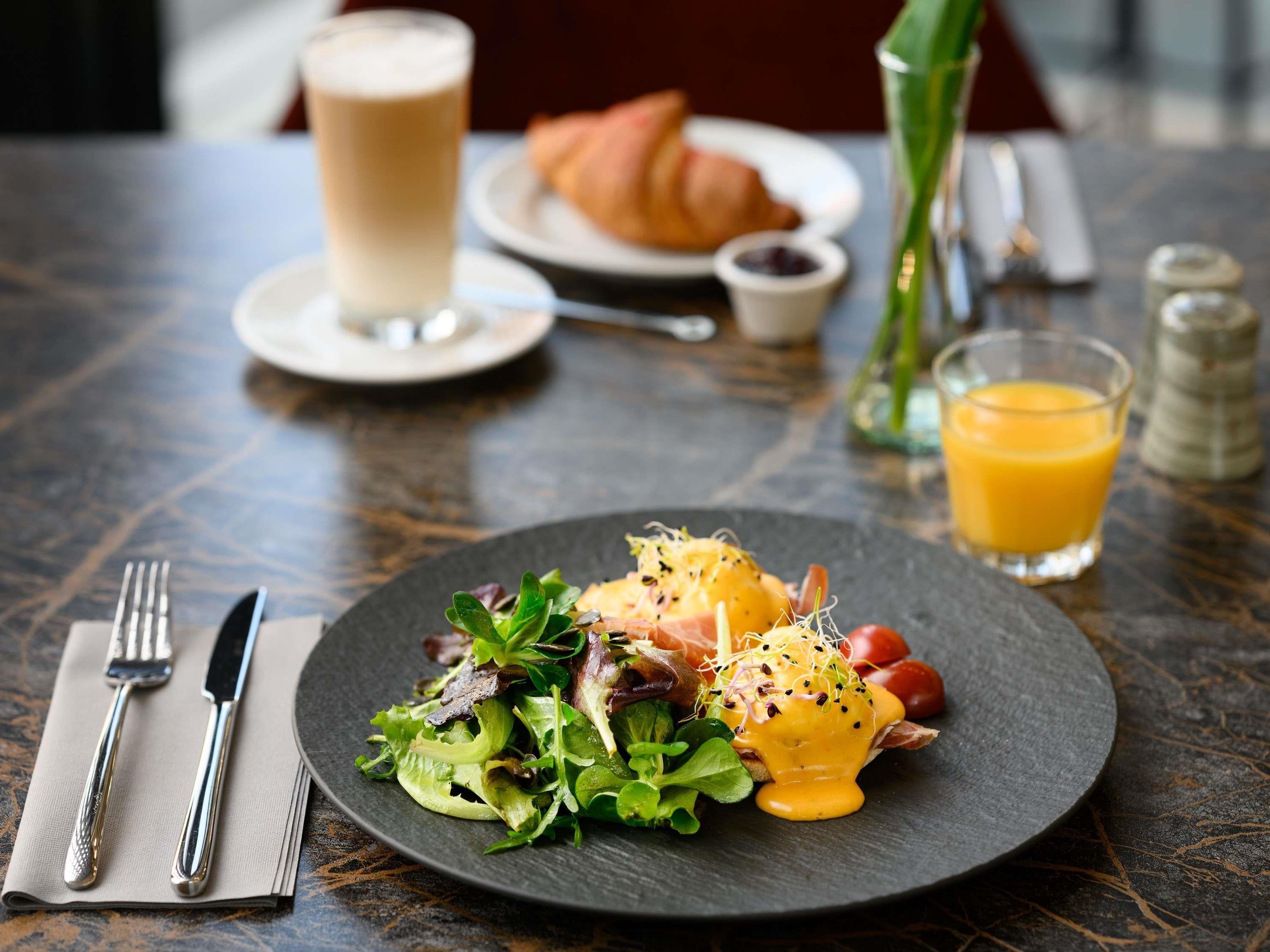 Una mesa de comedor con un plato de comida, un vaso de jugo de naranja, un croissant y una taza de café.