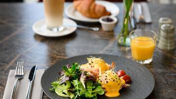 Una mesa de comedor con un plato de comida, un vaso de jugo de naranja, un croissant y una taza de café.
