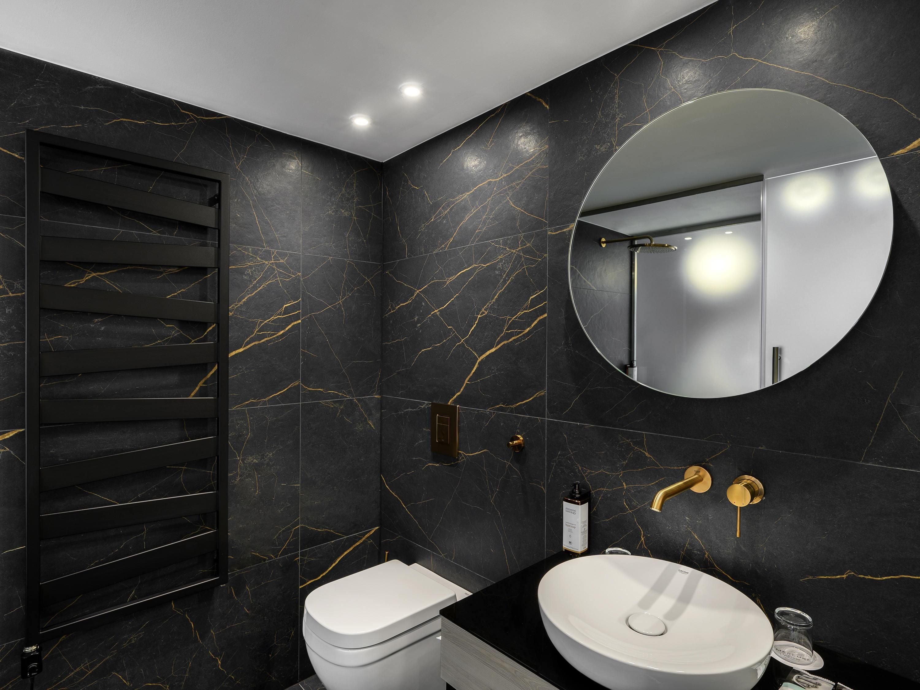 Un baño moderno con pared de mármol negro, un espejo redondo, un lavabo blanco y un inodoro.