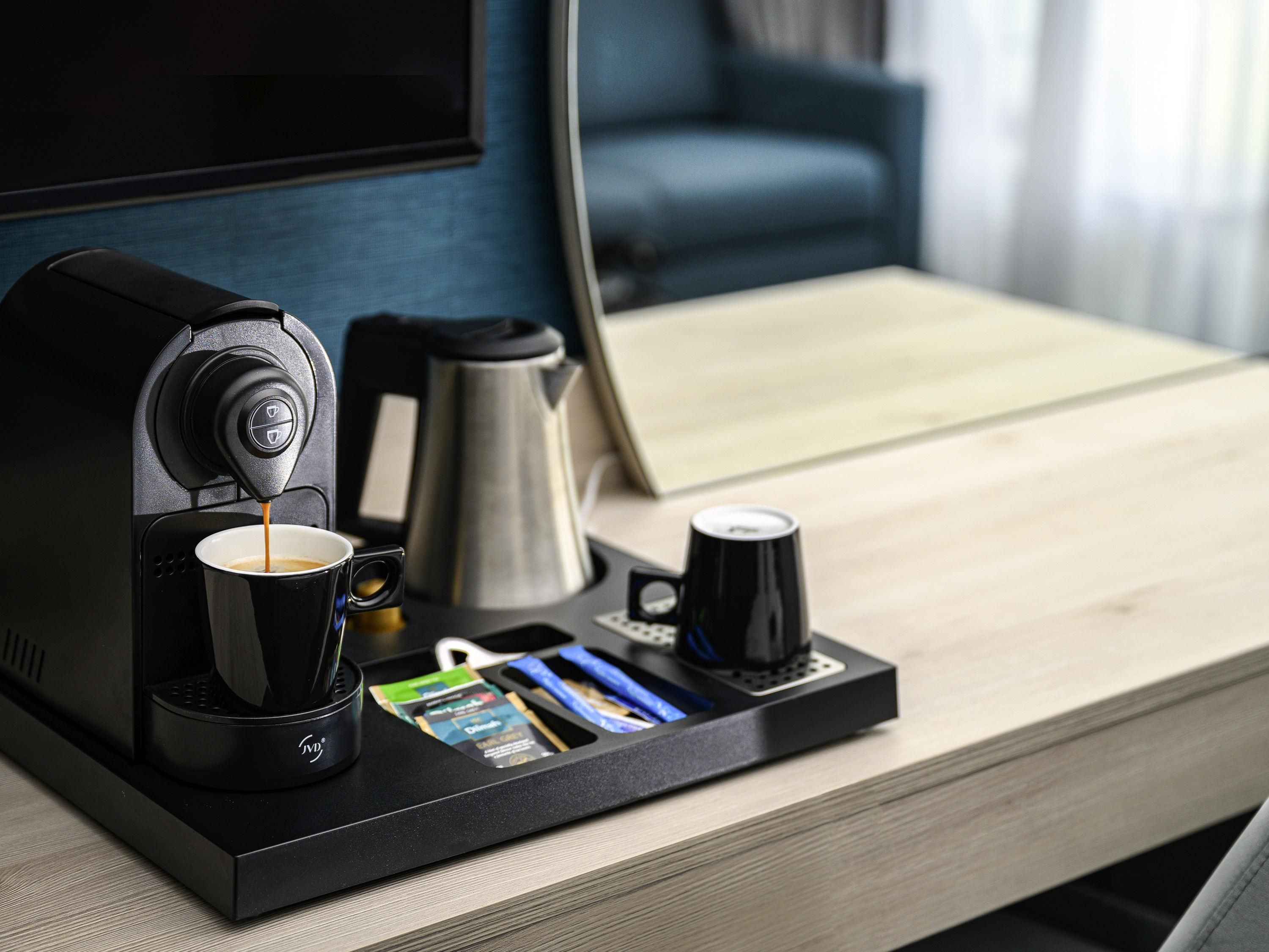 A coffee machine on a tray table with a cup of coffee, a coffee pot, and a mug.