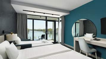 Una habitación de hotel moderna con dos camas, un escritorio, una silla, un espejo grande y vistas a un lago.