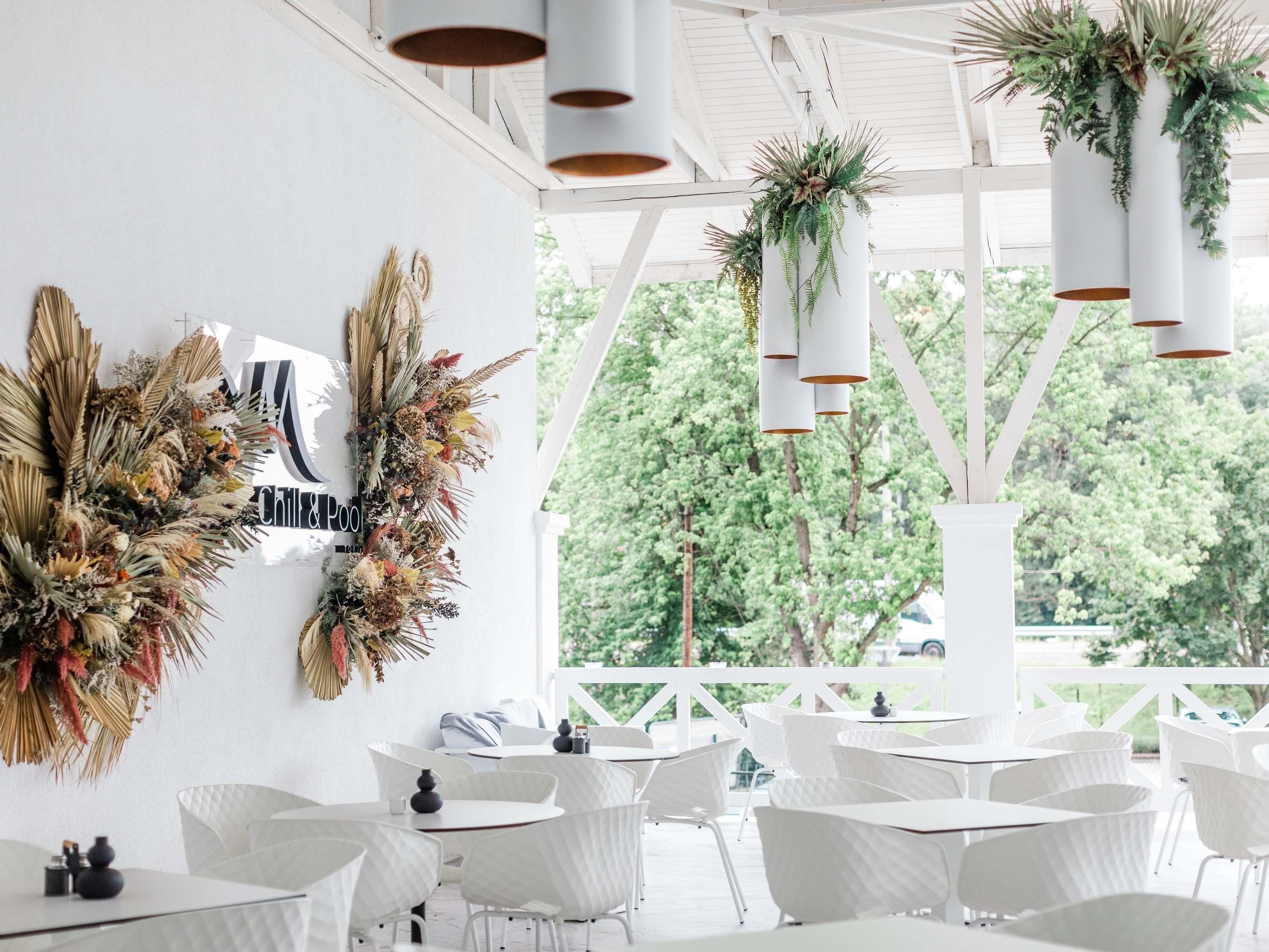 A restaurant with white chairs and tables, hanging plants, and a view of trees.