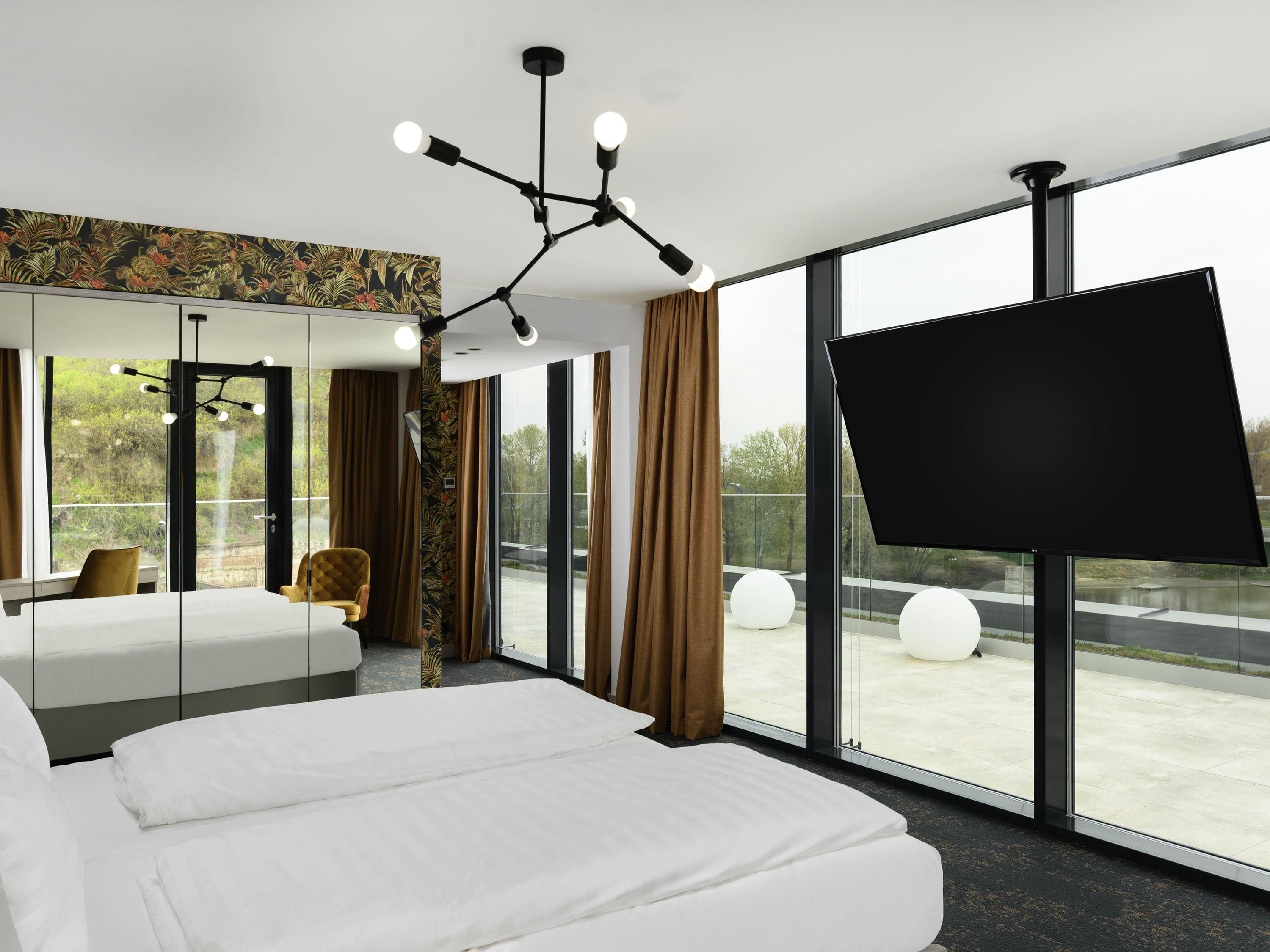 Quarto de hotel moderno com uma cama grande, área de estar, televisão e varanda com vista.