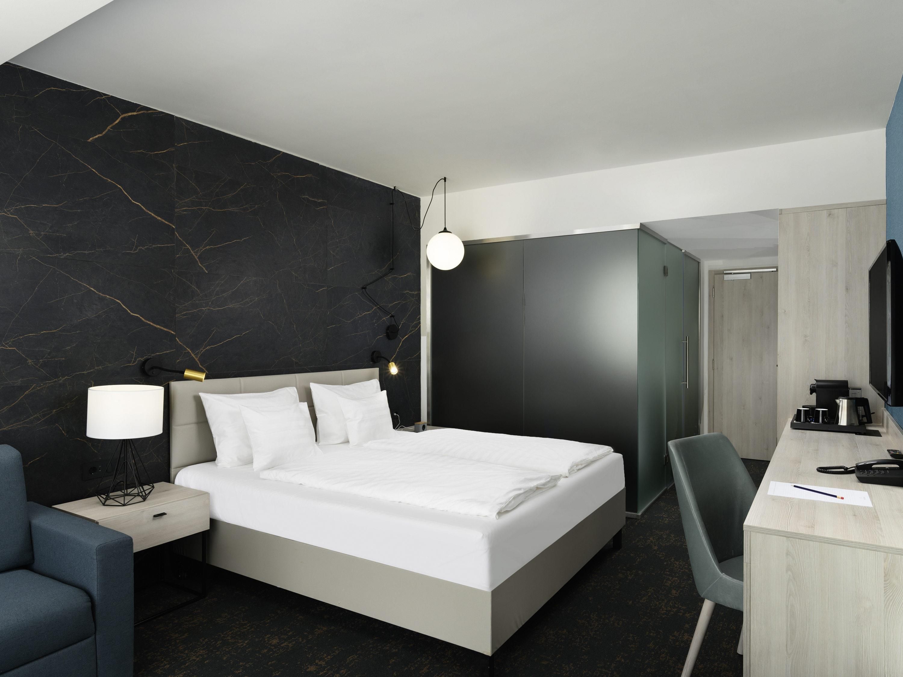 Una habitación de hotel moderna con una cama grande, mesita de noche, escritorio y silla.