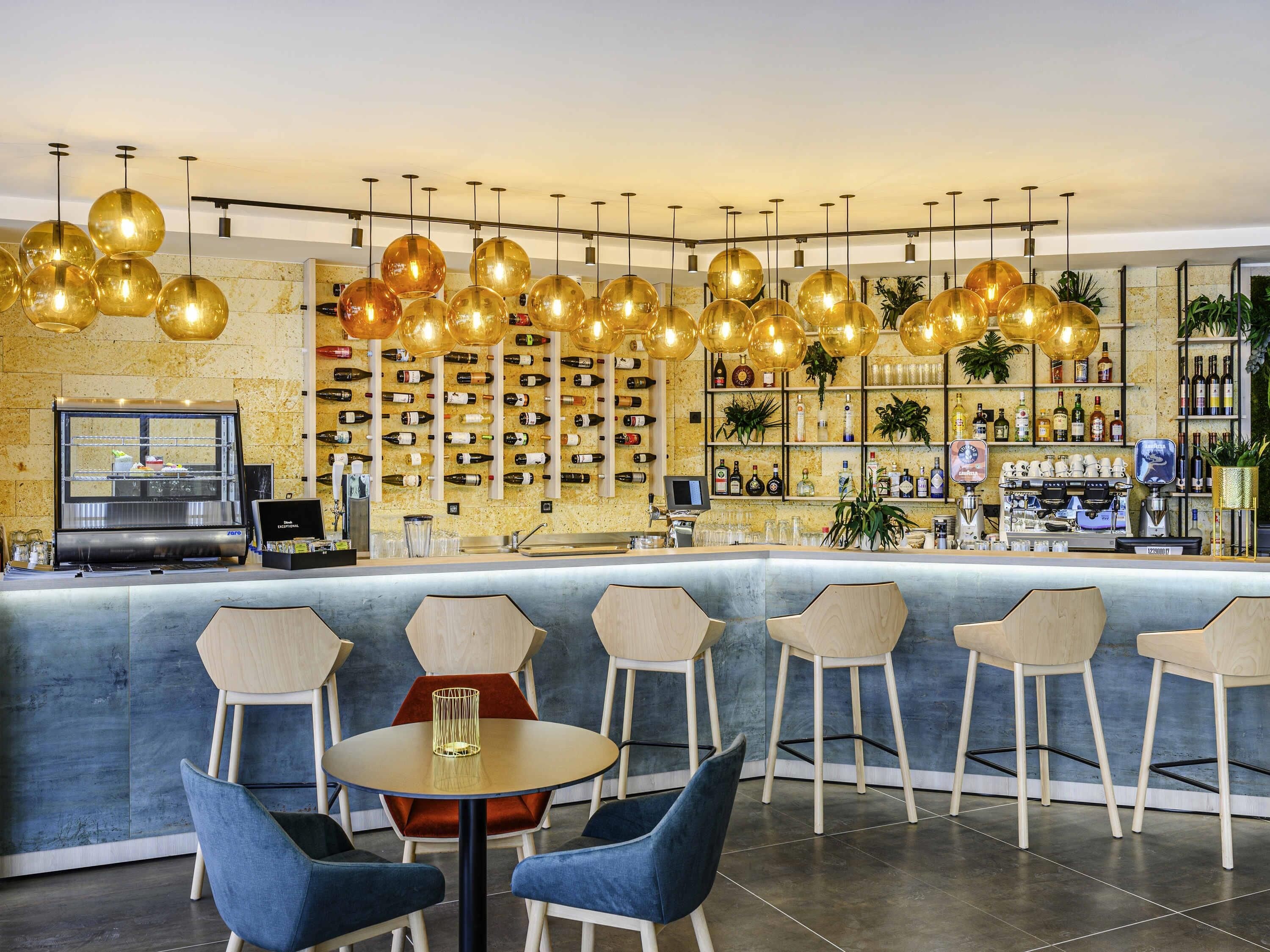 Zona de bar con mostrador, diversas opciones de asientos y una pared llena de botellas de vino.