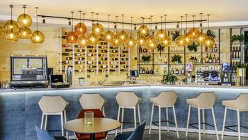 Zona de bar con mostrador, diversas opciones de asientos y una pared llena de botellas de vino.