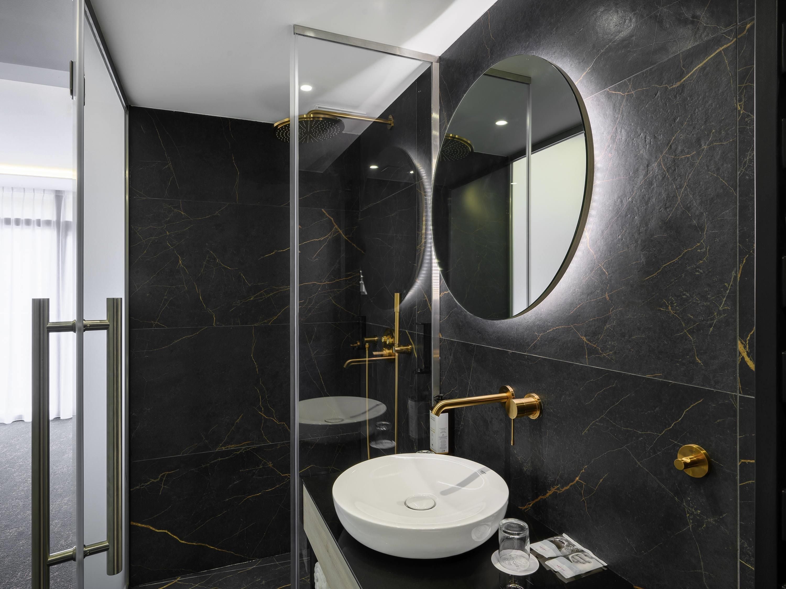A modern bathroom with a glass-enclosed shower, a round mirror, and a white sink.