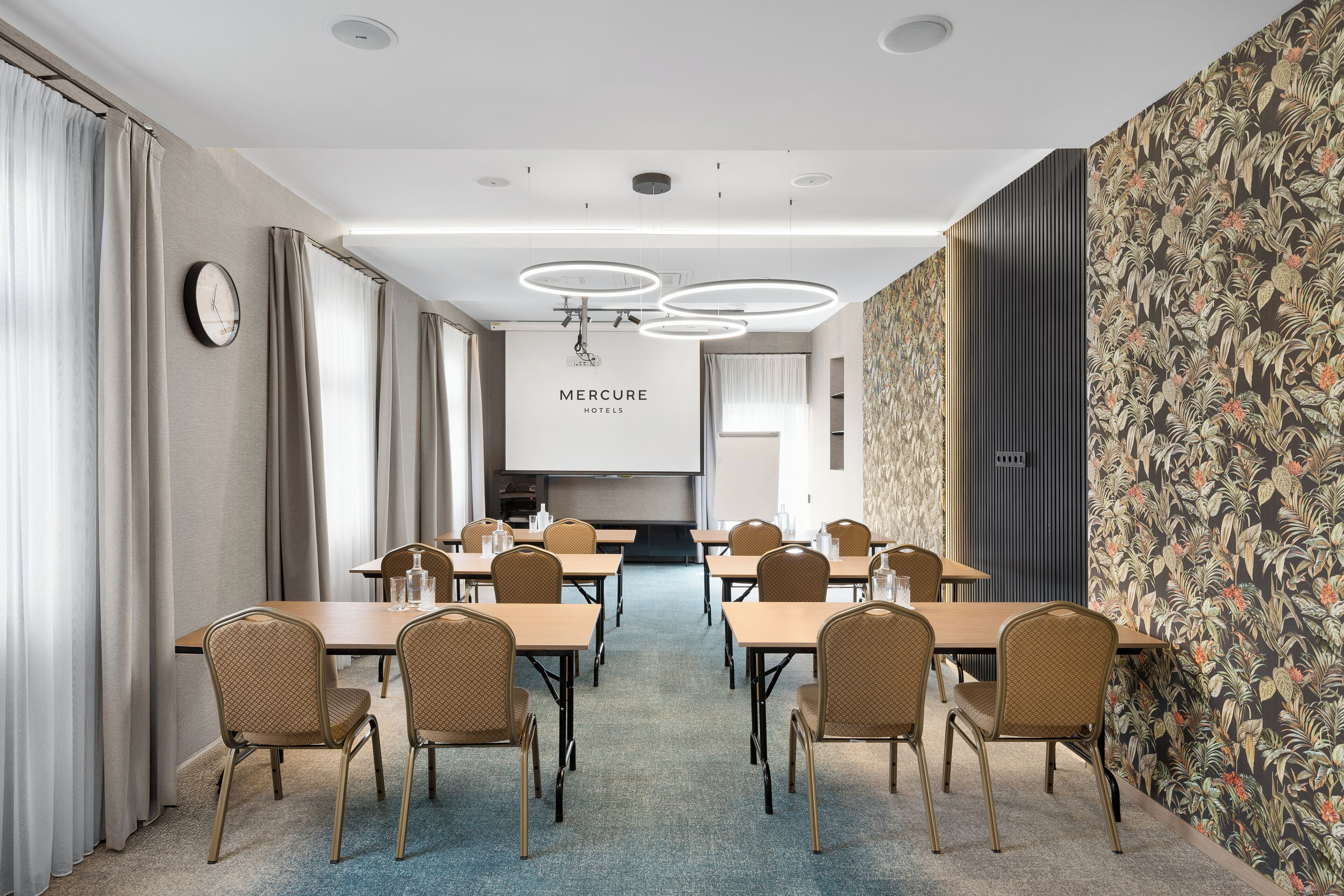 A conference room with tables and chairs, a clock, and a 'Mercure Hotels' sign.