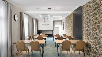 A conference room with tables and chairs, a clock, and a 'Mercure Hotels' sign.