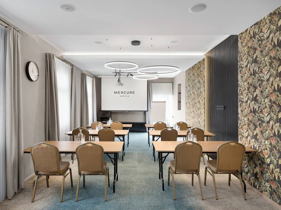 A conference room with tables and chairs, a clock, and a 'Mercure Hotels' sign.