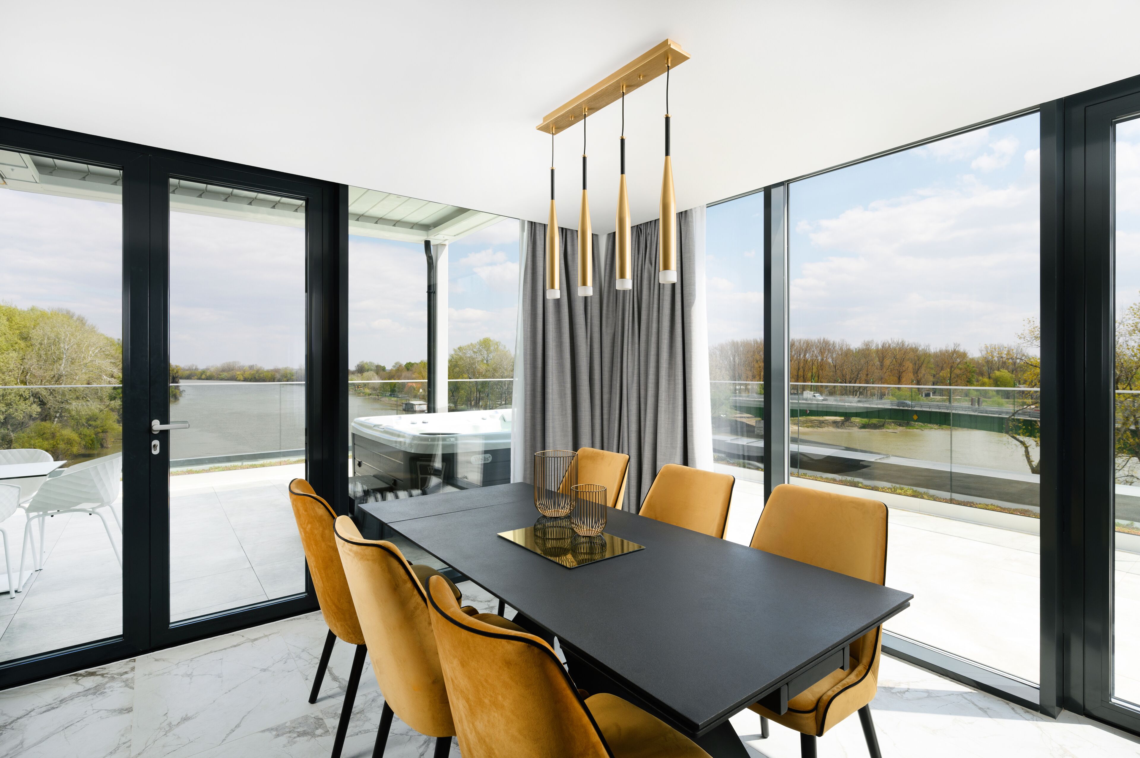 Een moderne eetruimte met een zwarte tafel, gele stoelen en uitzicht op een rivier door grote ramen.