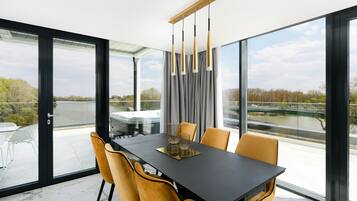 Een moderne eetruimte met een zwarte tafel, gele stoelen en uitzicht op een rivier door grote ramen.
