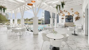 A spacious outdoor patio with white furniture, a pool, and a view of a modern building. - Mercure Tokaj Center (Tokaj)