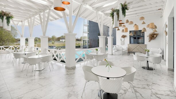 A spacious outdoor patio with white furniture, a pool, and a view of a modern building. - Mercure Tokaj Center (Tokaj)