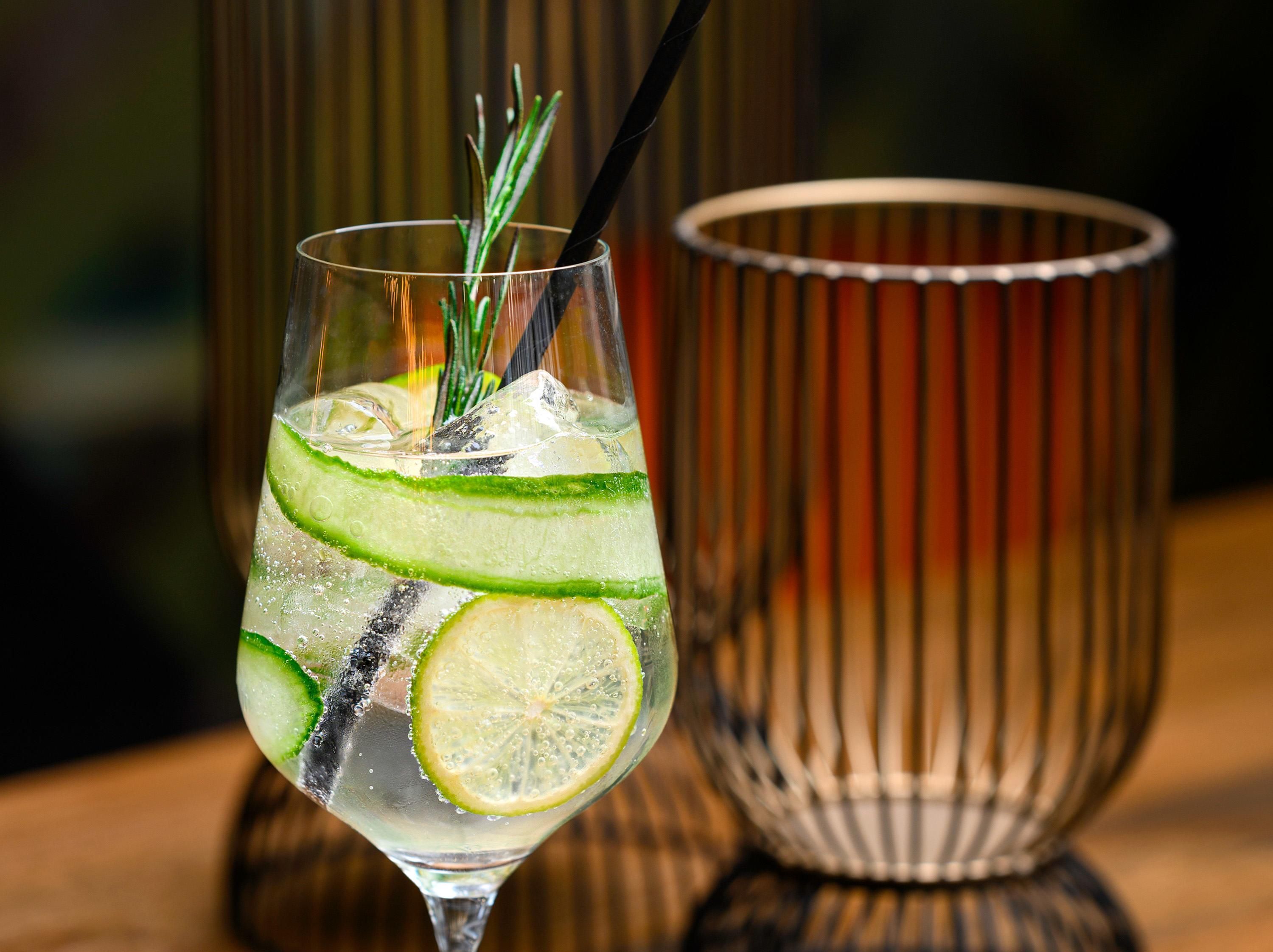 Een cocktailglas met limoenpartjes en een rietje, samen met een gestreepte glazen houder.