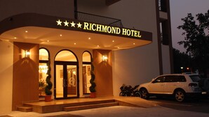 The exterior of Richmond Hotel with a well-lit entrance, a parking area, and a white SUV parked outside. - Richmond Hotel (Constanta)