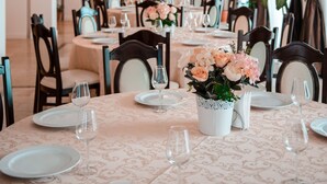 A dining area with round tables set for a meal, featuring a chandelier, floral centerpieces, and dark curtains. - Richmond Hotel (Constanta)