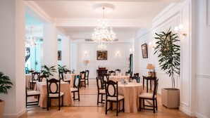 A formal dining room with round tables, chairs, and a chandelier. - Richmond Hotel (Constanta)