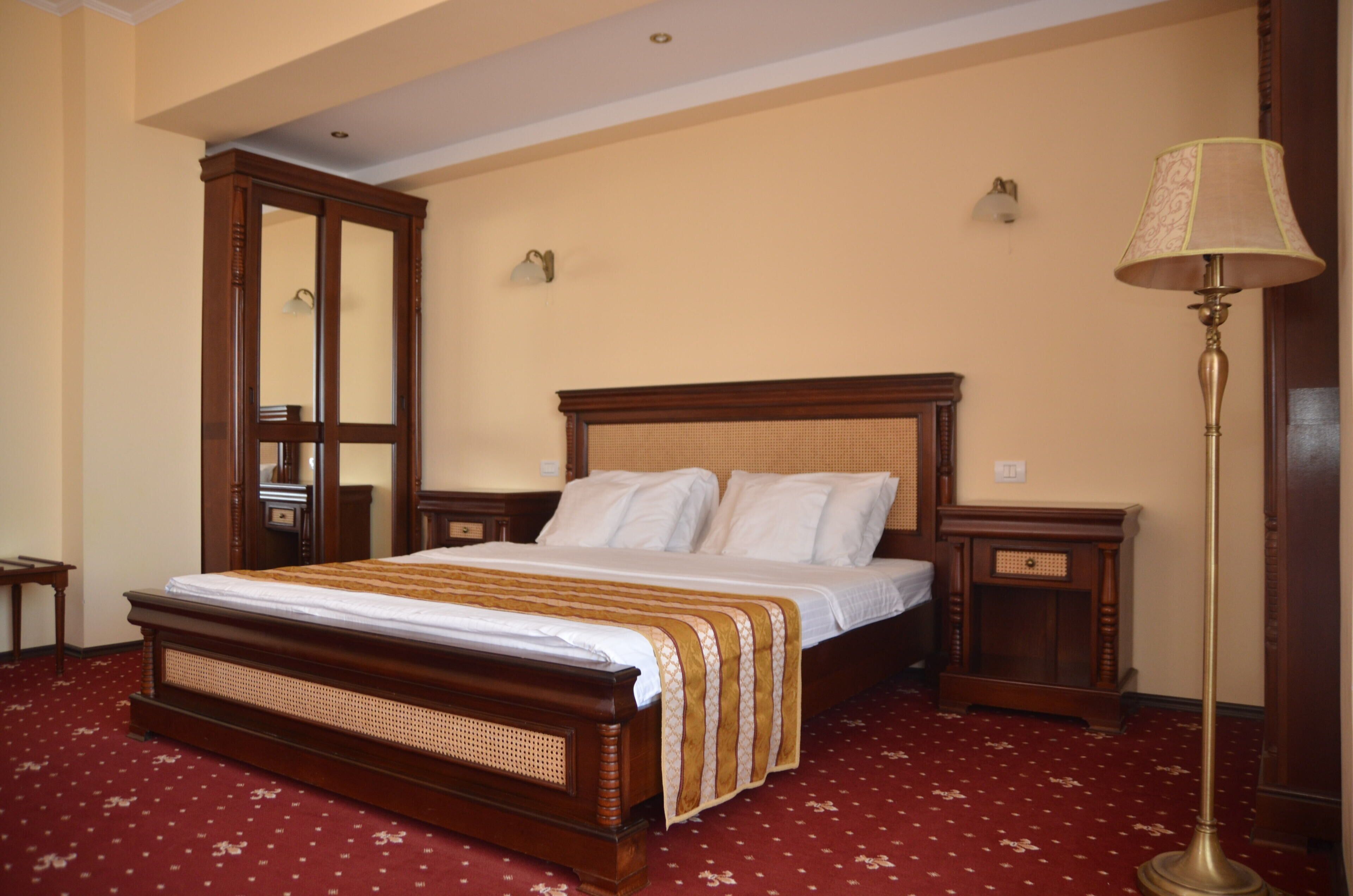 Une chambre d’hôtel avec un grand lit, une tête de lit en bois, deux tables de chevet, une lampe sur pied et un miroir.