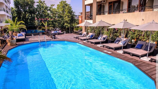 A swimming pool with lounge chairs and umbrellas, surrounded by greenery and buildings. - Richmond Hotel (Constanta)