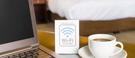 Una computadora portátil, un cartel de acceso a Wi-Fi y una taza de café sobre una mesa en una habitación de hotel.