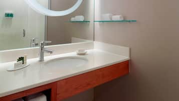 A bathroom with a white sink, a mirror, and a glass shelf with toiletries.
