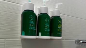 Tres botellas de champú y acondicionador Tea Tree Special sobre un estante blanco.
