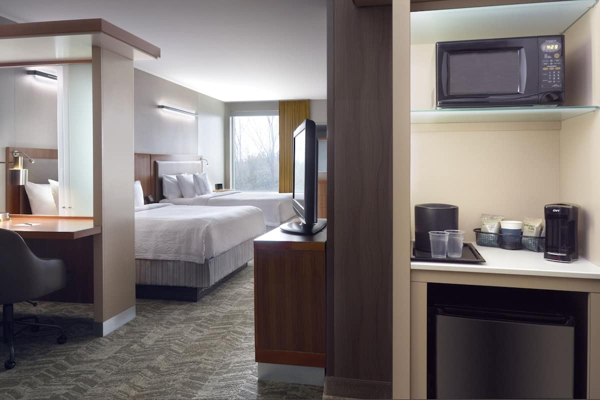 A hotel room with a bed, desk, chair, television, microwave, and a small kitchenette area.