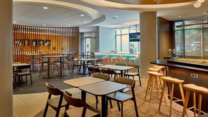 A modern restaurant with a variety of seating options, including tables and bar stools, and a large window offering a view of the outdoors.